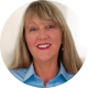 Angela Main Roberts Smiling woman with long blonde hair wearing a light blue shirt, posed against a light background.