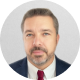 David Sims Headshot of a man in a suit and red tie with a short beard, set against a light gray background.
