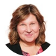 lynn-mayer A woman with wavy, light brown hair smiles at the camera. She is wearing a patterned top with a dark jacket. The background is plain white.