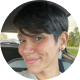 Nat Valentin Heaney A woman with short dark hair smiles slightly while sitting in a car, with trees visible through the window in the background.